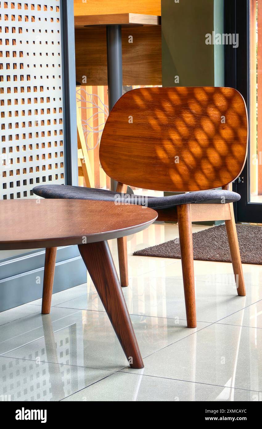 Mid-century modern furniture: Elegant wooden chair and coffee table in sunlit interior with perforated screen and warm tones Stock Photo