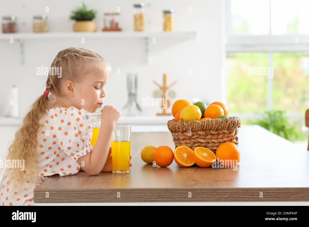 Cute little girl drinking orange juice in kitchen Stock Photo - Alamy