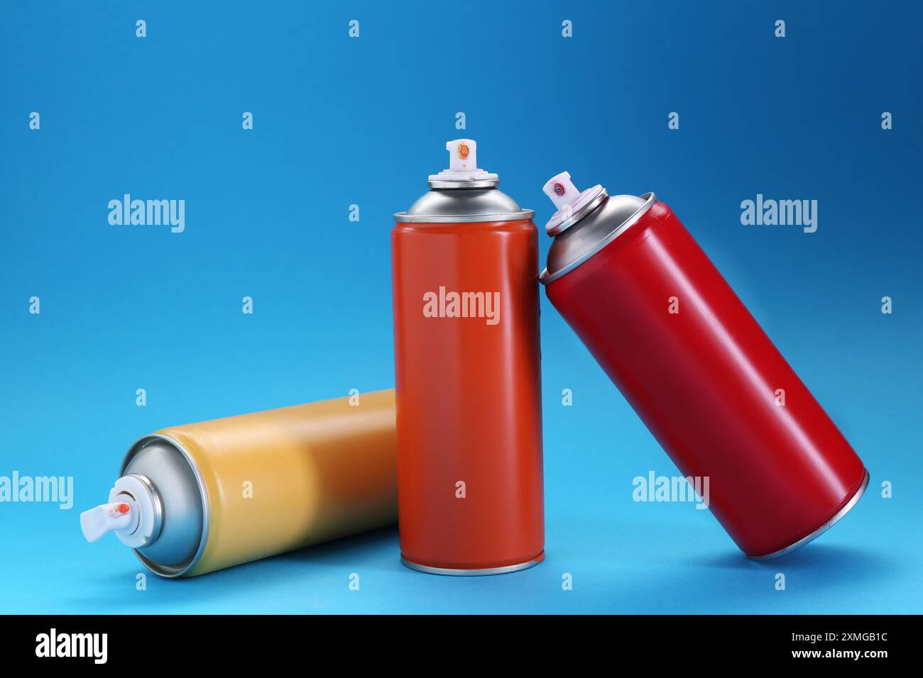 Three spray paint cans on light blue background Stock Photo - Alamy