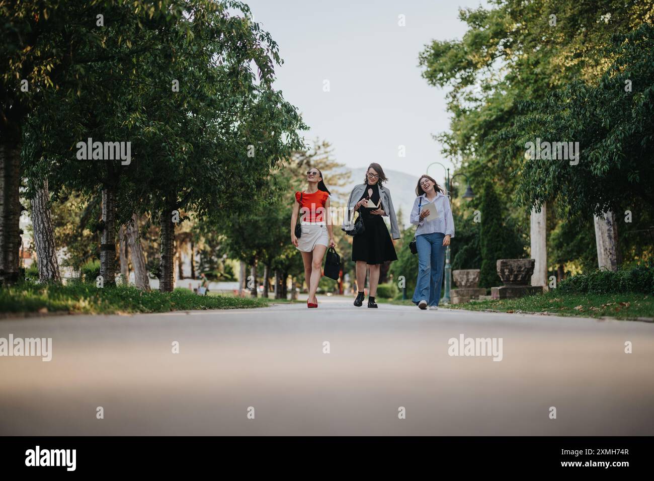 Three businesswomen walking and talking in a park, enjoying the ...