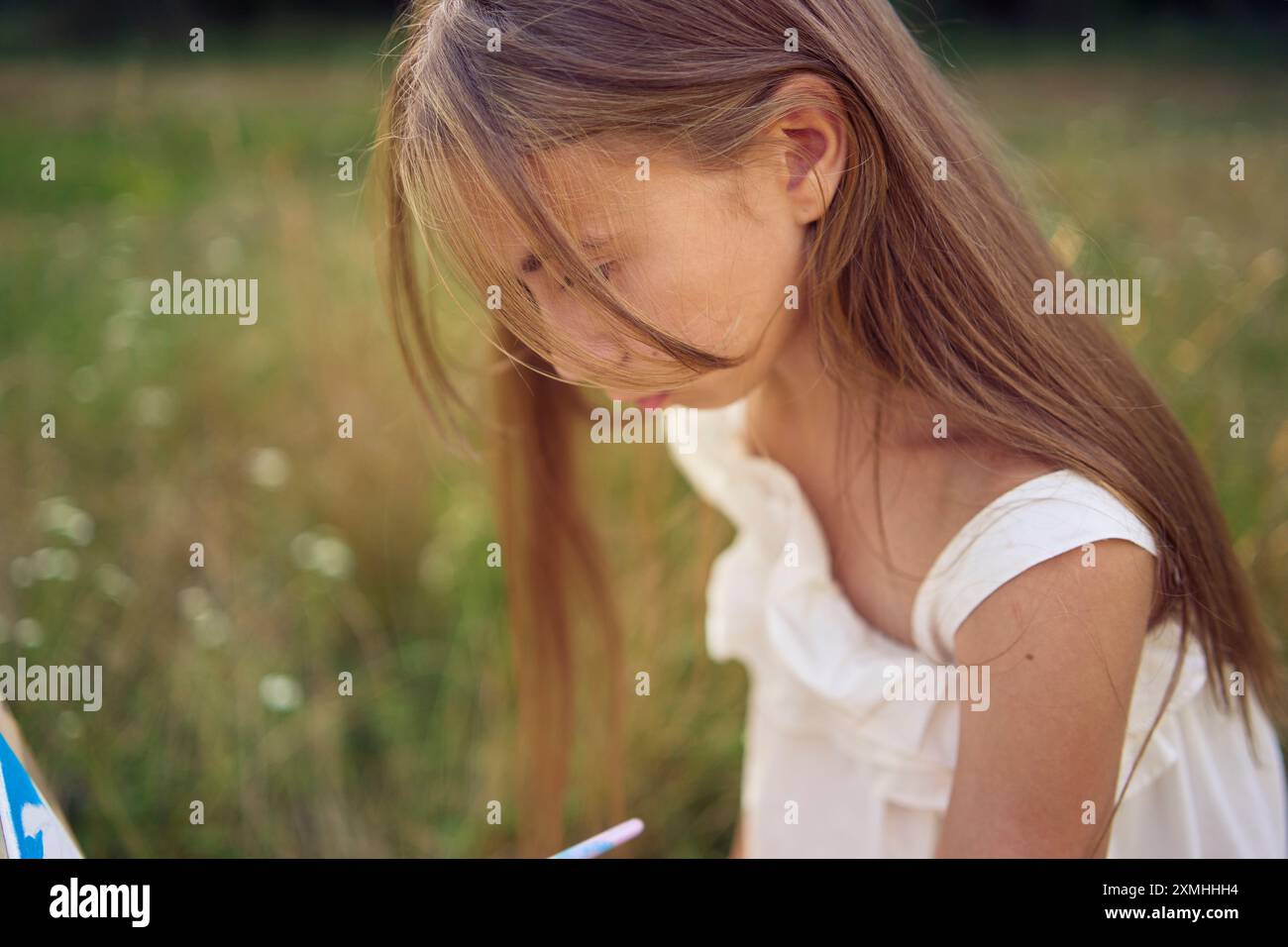 a pre-teen girl in a summer dress paints a picture in the garden on an ...