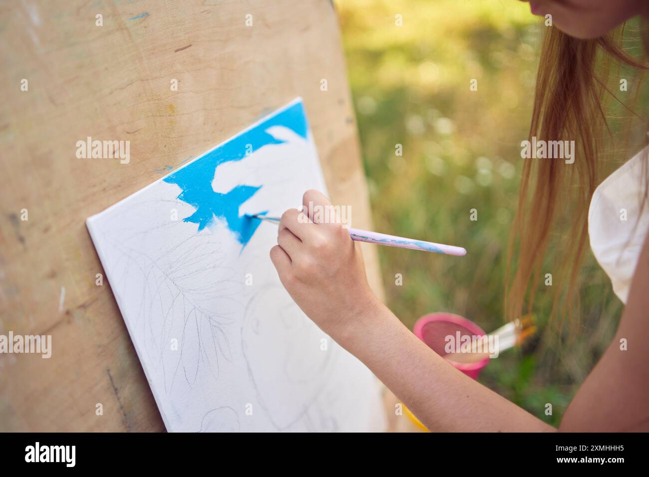 a pre-teen girl in a summer dress paints a picture in the garden on an ...