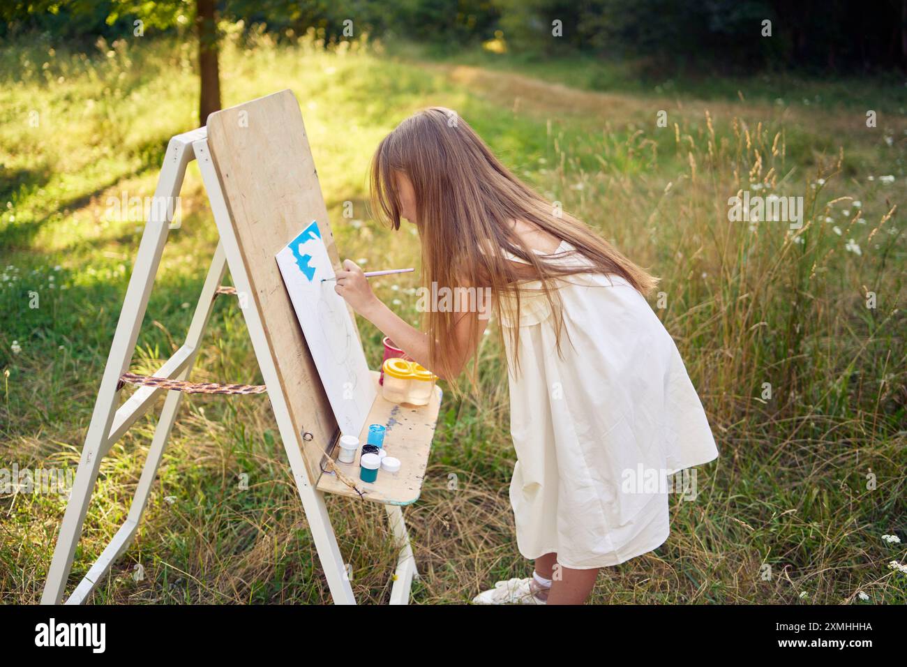 a pre-teen girl in a summer dress paints a picture in the garden on an ...
