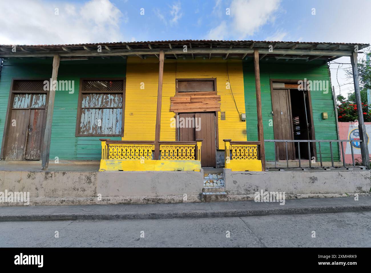 557 Green and yellow facade of wood, one-storey old Colonial house with entrance porch on timber columns, 33-35 Calle Maceo Street. Baracoa-Cuba. Stock Photo