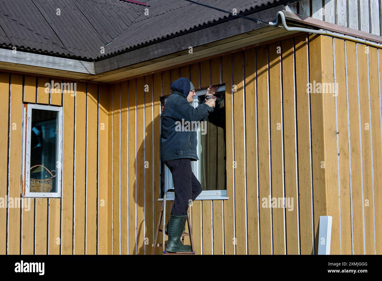 Outdoor work on window openings, roofer installs metal window slopes on facade of frame panel country house. Stock Photo