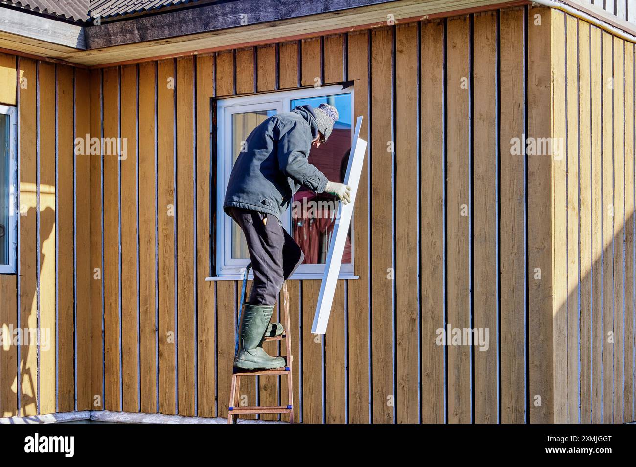 Standing on stepladder, roofing contractor installs metal window slopes on facade side. Stock Photo