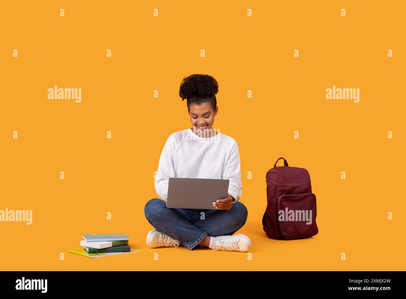 Young Woman Using Laptop While Sitting On Yellow Background Stock Photo