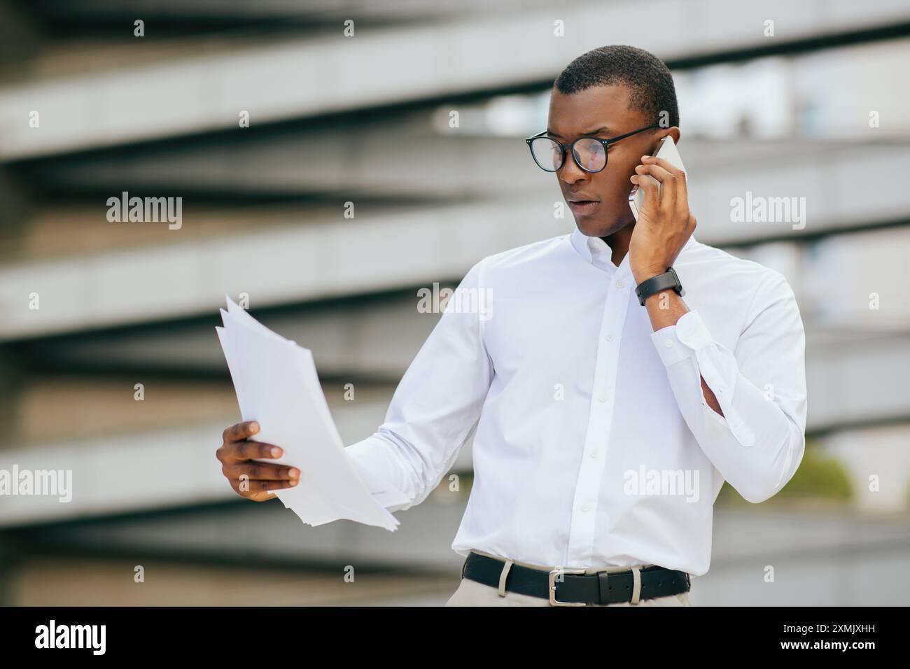 Businessman Talking On Phone While Reviewing Documents Outdoors Stock Photo