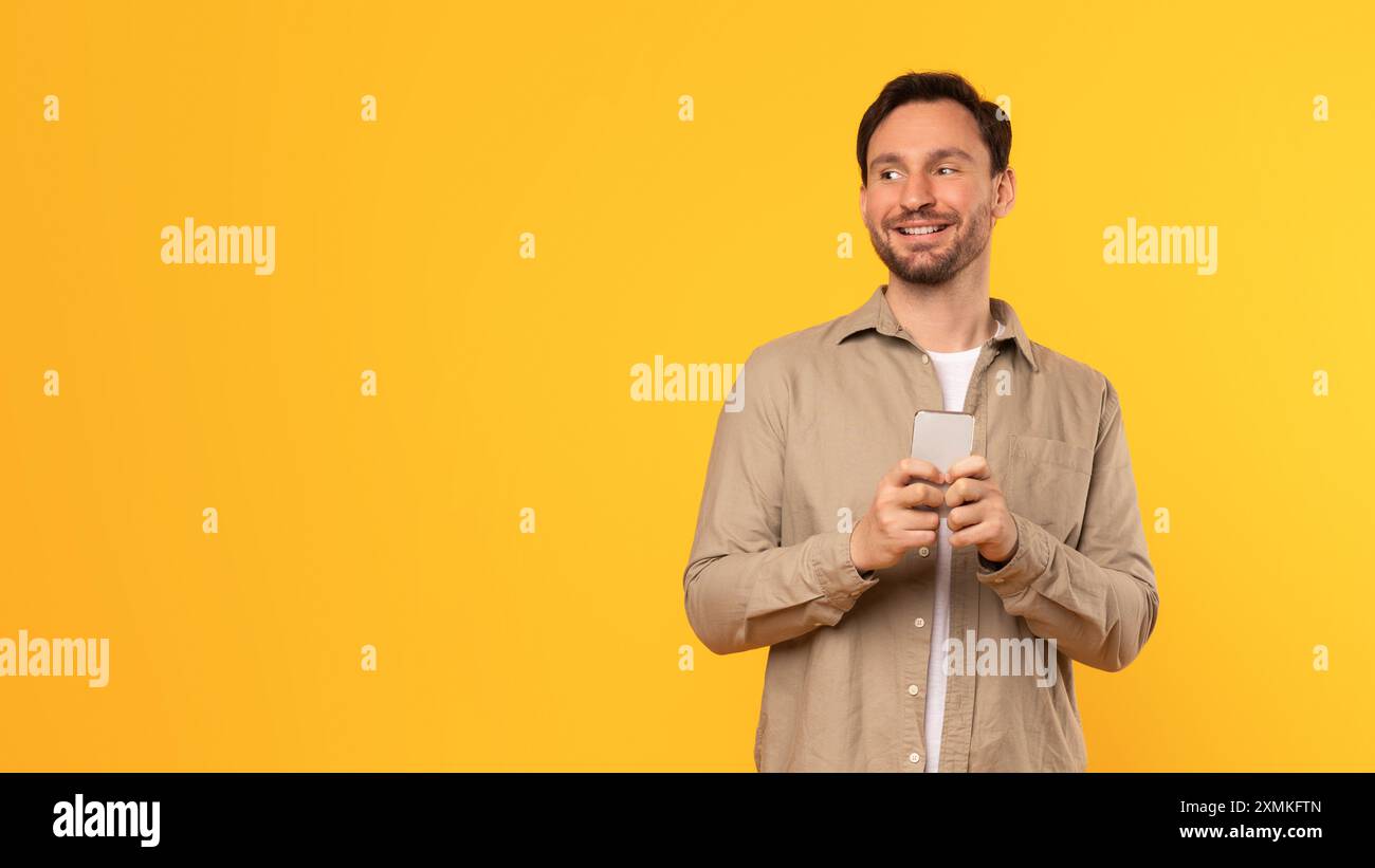 Happy Man Using Smartphone Against Yellow Background Stock Photo
