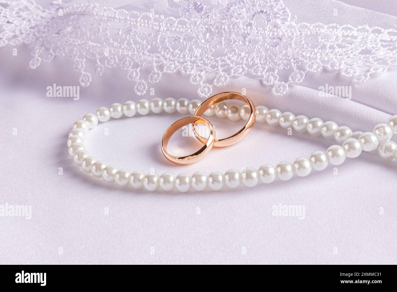 Two gold wedding rings lie on a string of pearl beads. on a white satin ...