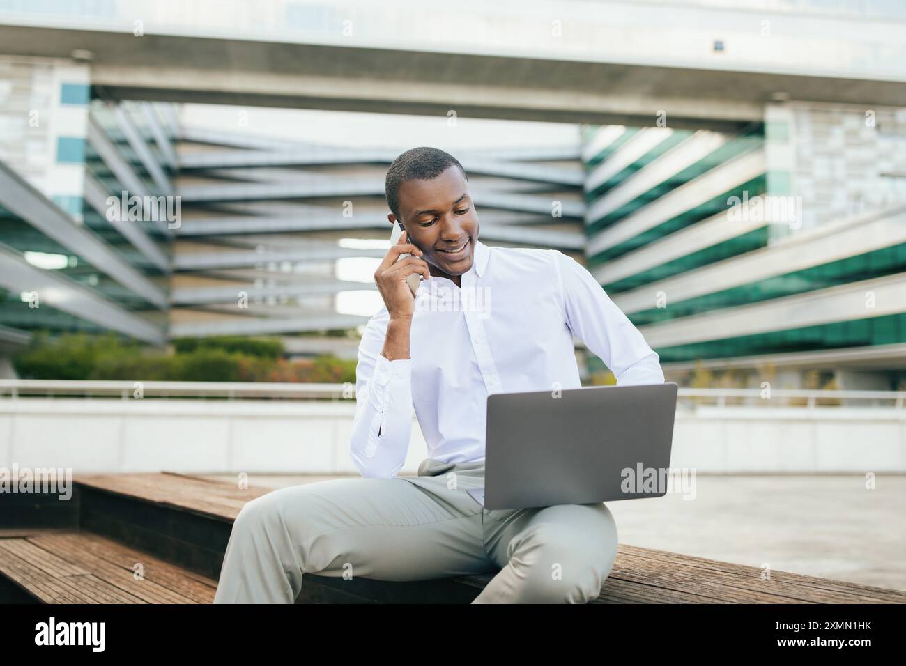 Man Talking on Phone While Working on Laptop Outside Building Stock Photo