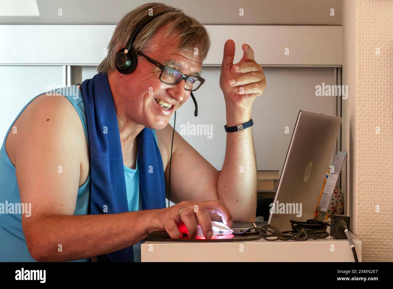 Älterer Mann schwitzt im Home Office, leidet unter Hitze in der Dachwohnung, München, Ende Juli 2024 Deutschland, München, Juli 2024, Mann schwitzt im Home Office, leidet unter Hitze in der Dachwohnung, sitzt unter der Dachschräge, sitzt im Unterhemd im Büro, er telefoniert und arbeitet am Computer, trägt ein Headset, das Notebook vor sich auf dem kleinen Schreibtisch, unpassende Kleidung für Videokonferenzen, Silver Worker, älter, Boomer, privat, Arbeitszeit, Brille, Wohnung, Bayern, *** Older man sweats in home office, suffers from heat in attic apartment, Munich, end of July 2024 Germany, M Stock Photo