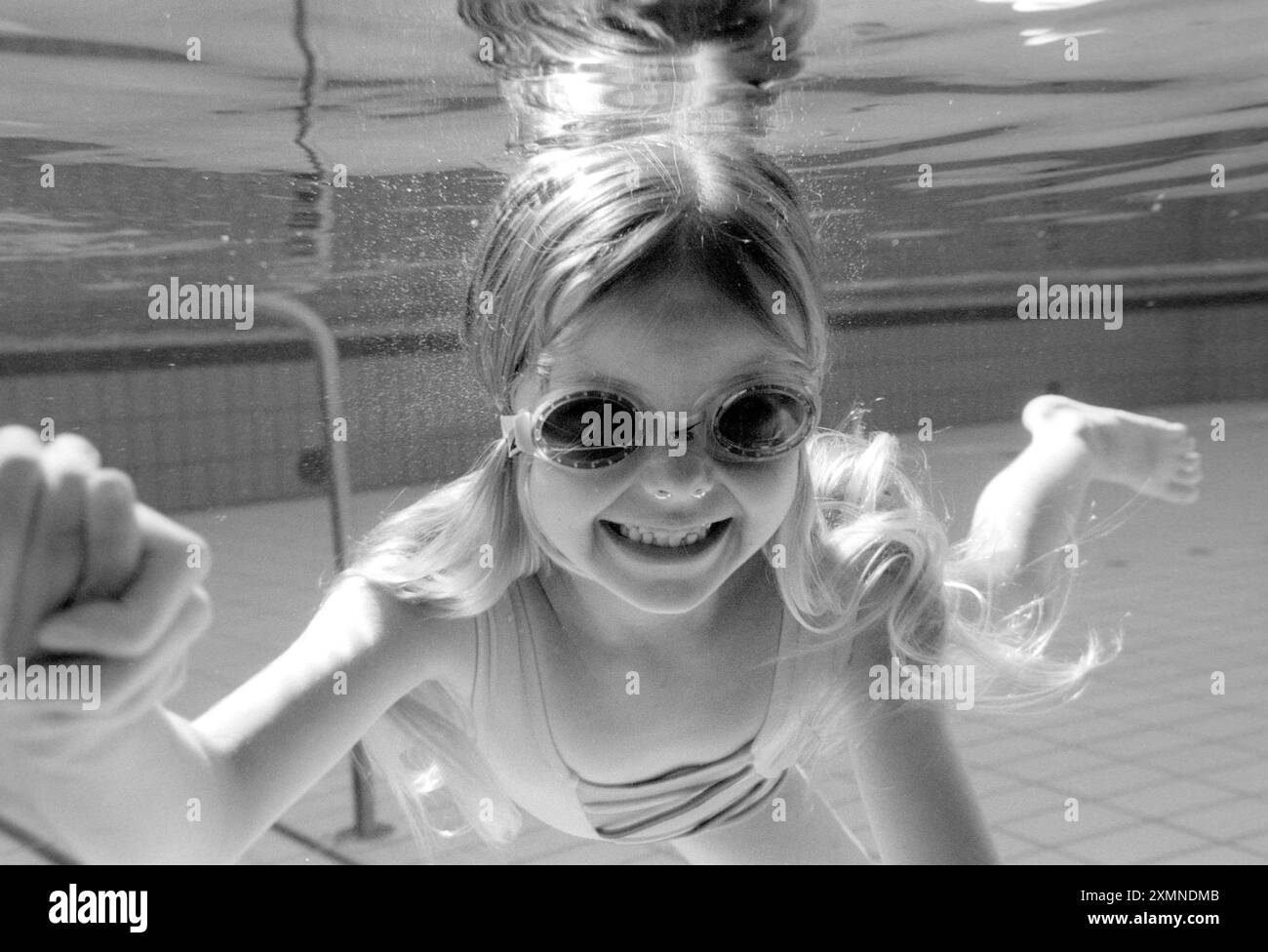 Girl swimming underwater in a swimming pool wearing goggles and smiling ...