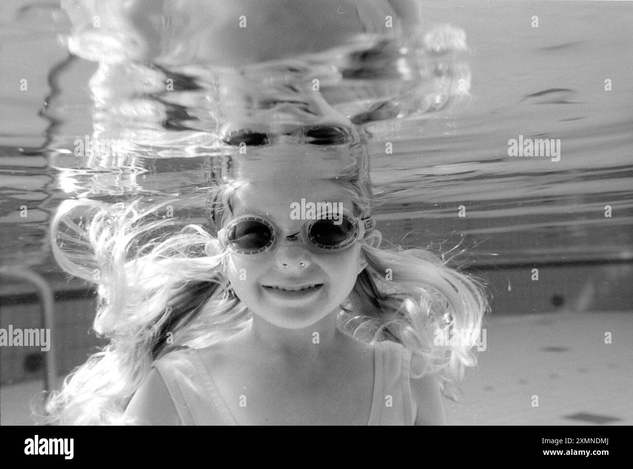Girl swimming underwater in a swimming pool wearing goggles and smiling ...