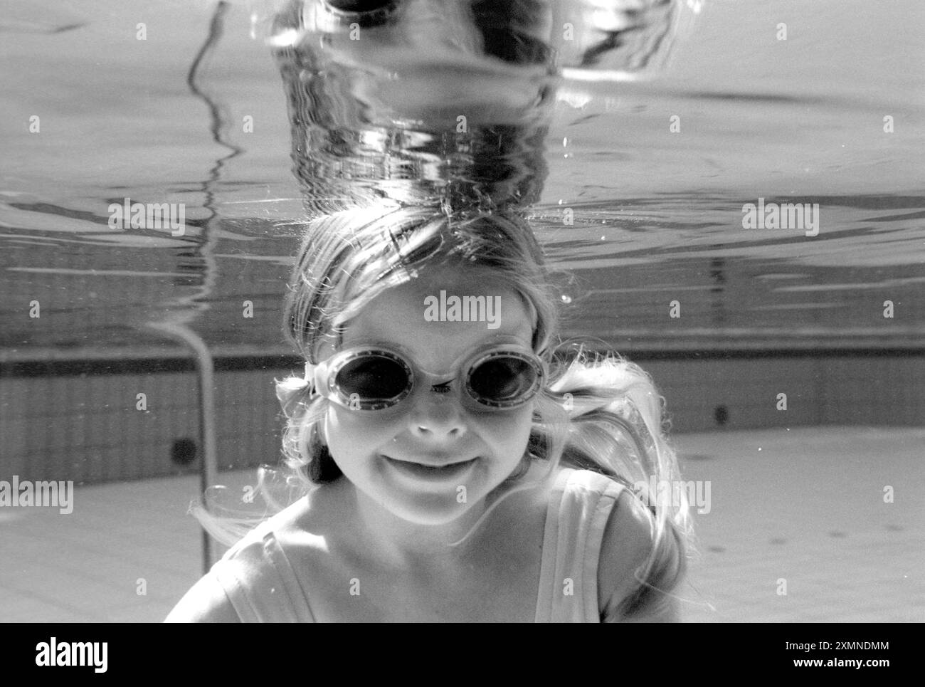 Girl swimming underwater in a swimming pool wearing goggles and smiling ...