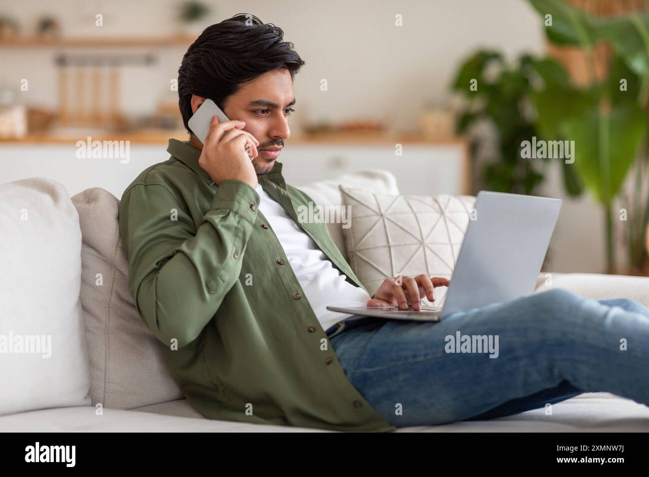 Young Man Talking on Phone While Working on Laptop Stock Photo