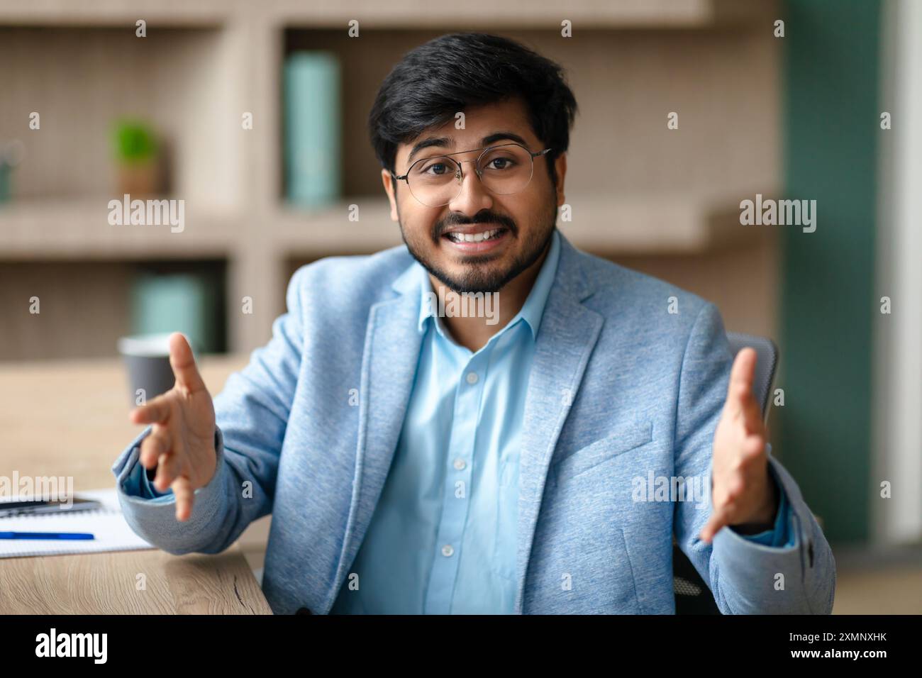 Smiling Man Gesturing While Sitting At Desk In Office Stock Photo
