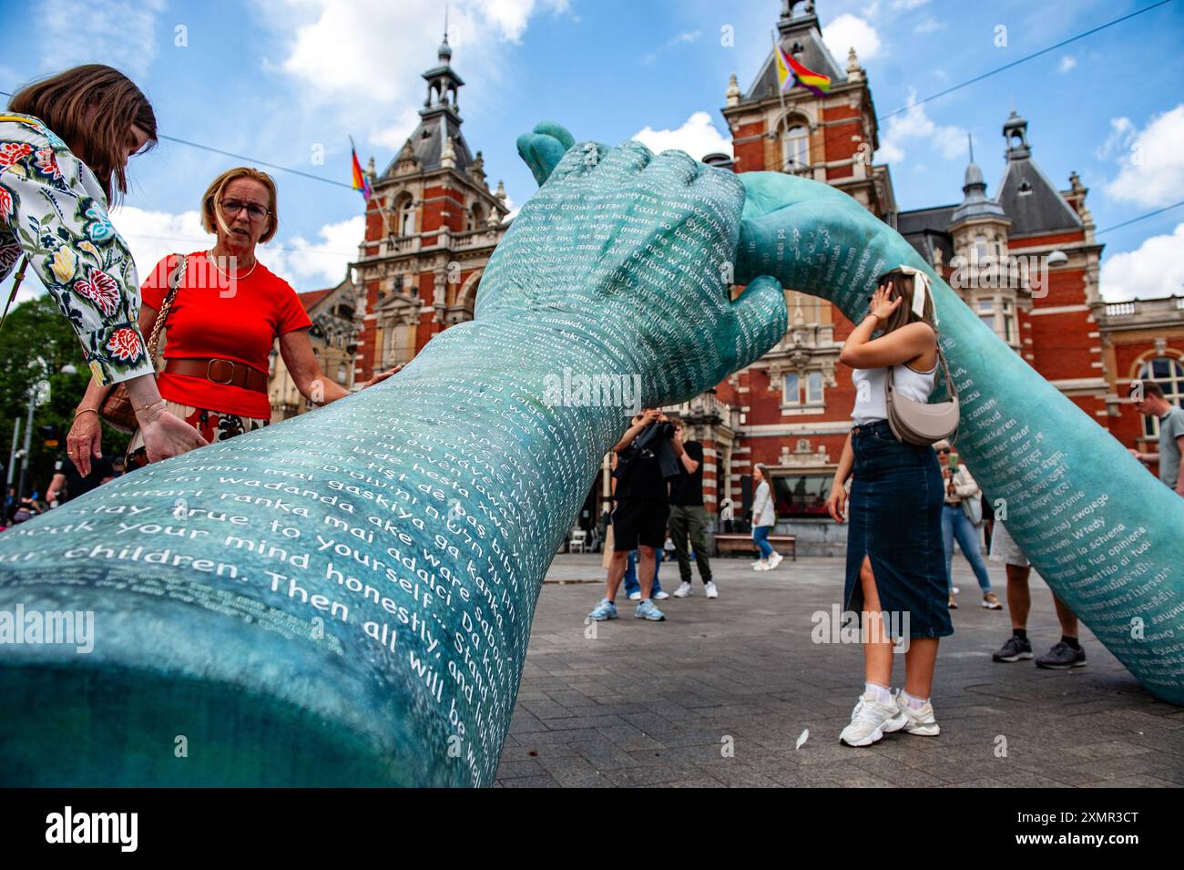 Amsterdam, Netherlands. 27th July, 2024. People are seen reading the text written over the big hands. Three years after the famous crime journalist Peter R. de Vries was murdered, a monument to honor his memory stands in the center of Amsterdam. The memorial, two bronze helping hands, not only memorializes the crime reporter and his work but also ensures that the 'inhuman crime' of his murder is not forgotten. Credit: SOPA Images Limited/Alamy Live News Stock Photo