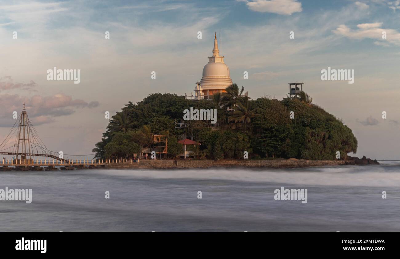 A serene view of the Paravu Duwa Pagoda on a lush island connected by a ...