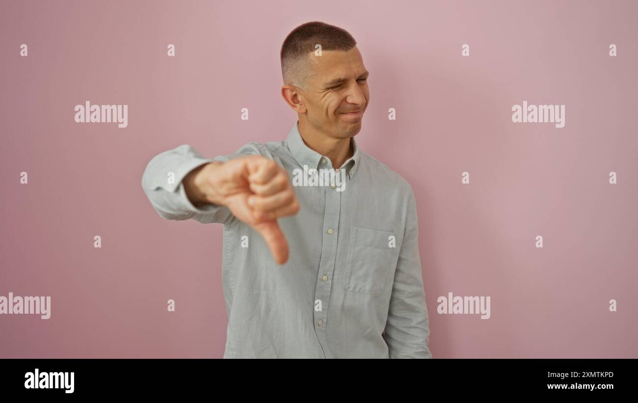 Young man giving a thumbs down isolated against a pink background ...