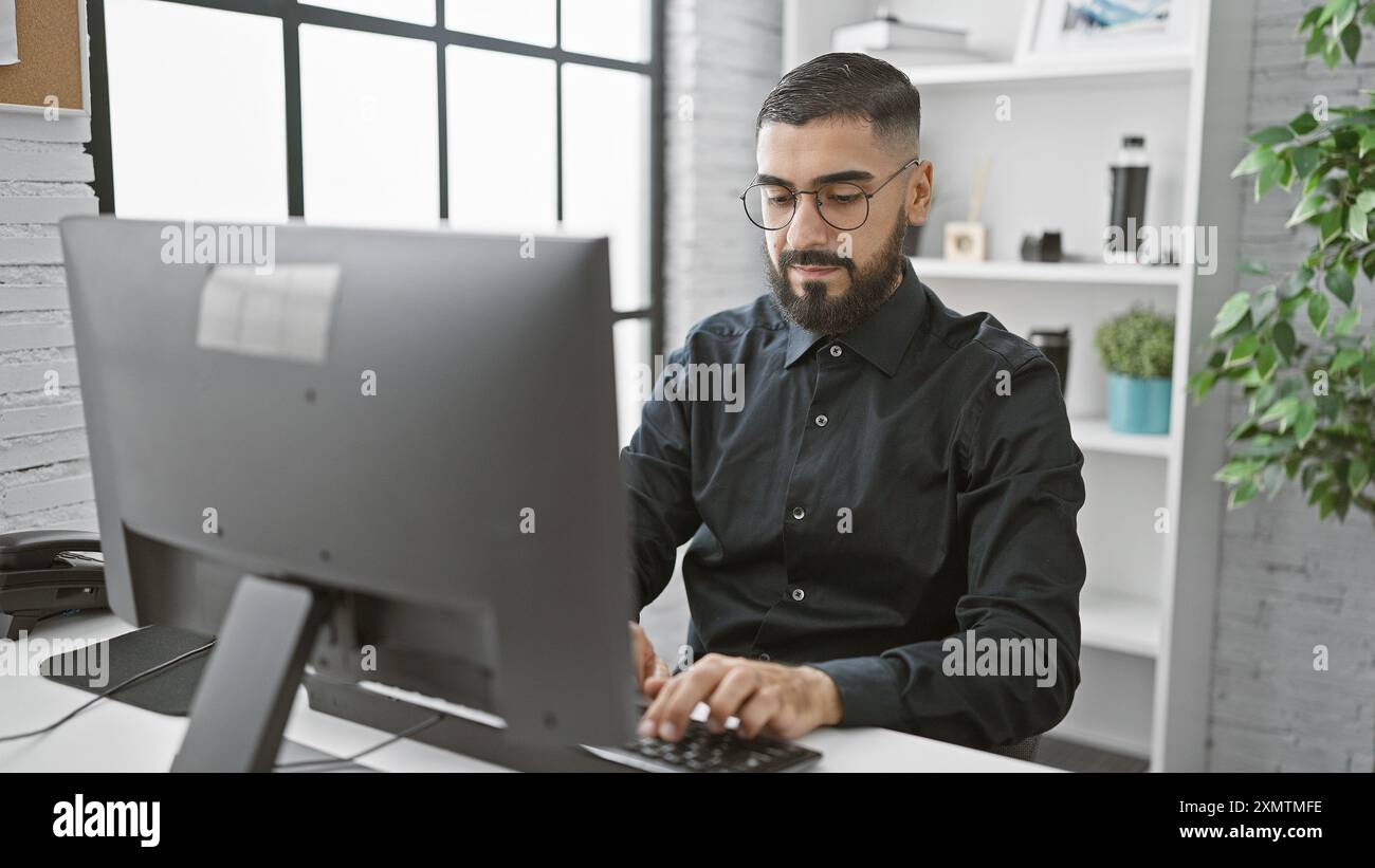 Handsome bearded man working intently on a computer in a modern office setting. Stock Photo