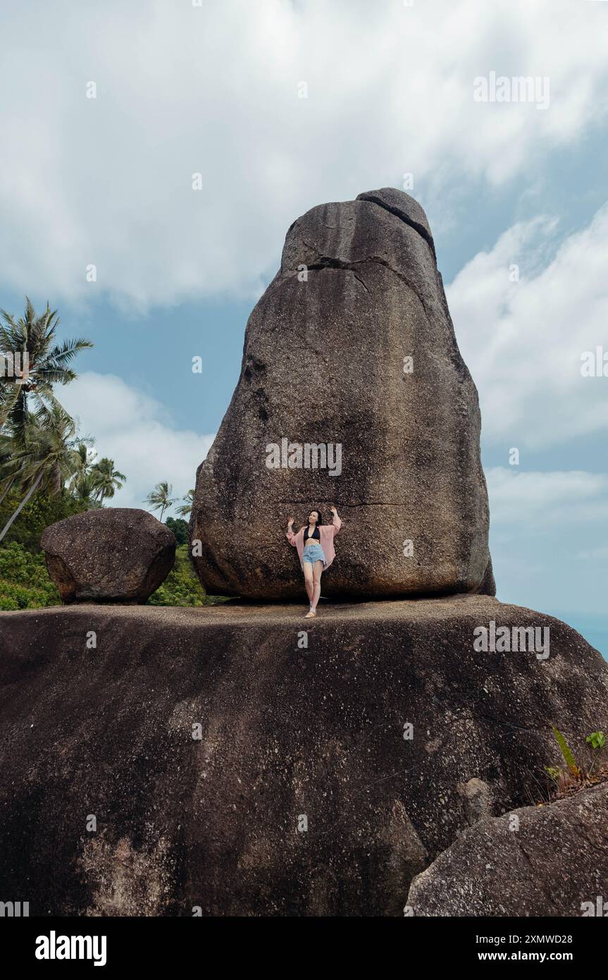 A woman stands on a large boulder, looking up at another massive rock formation. The rocks are known as Hin Ta Hin Yai, a popular tourist attraction o Stock Photo
