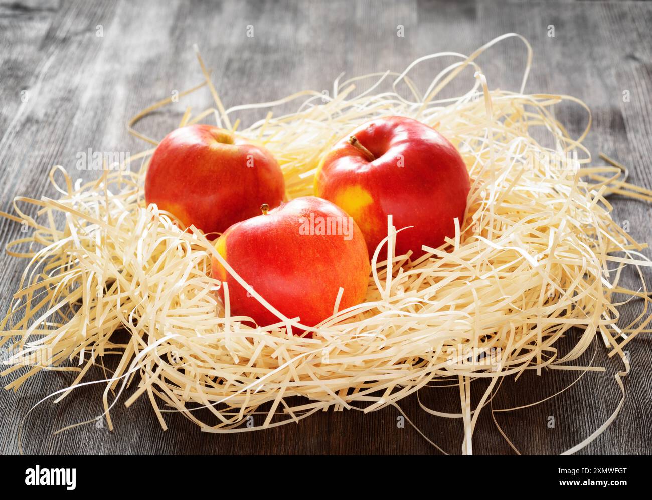 Three apples in straw on a table Stock Photo