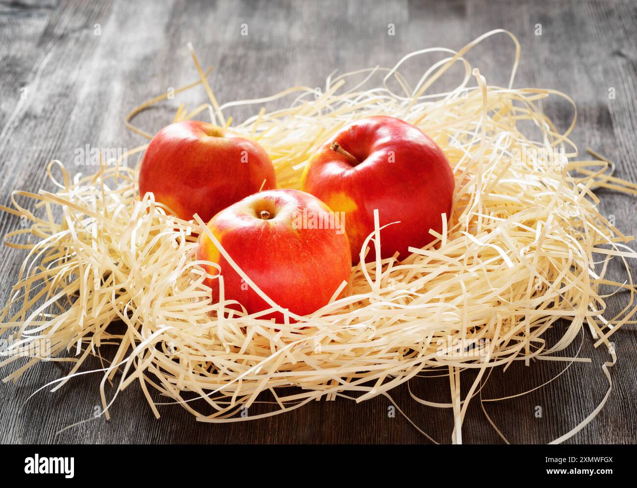 Three apples in straw on a table Stock Photo