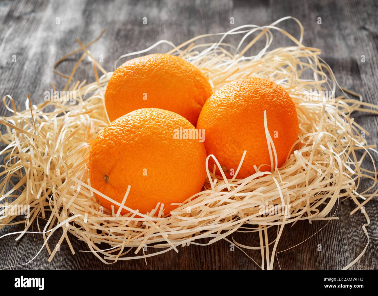 Three oranges in straw on a table. Stock Photo