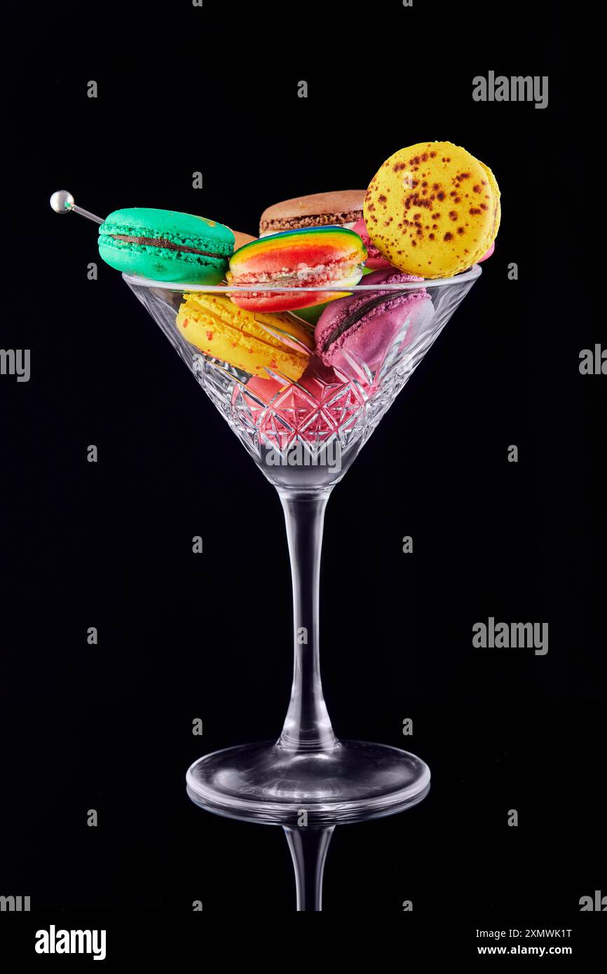 Vibrant, assorted macarons displayed elegantly in a martini glass against a black background, showcasing a creative dessert presentation. Stock Photo