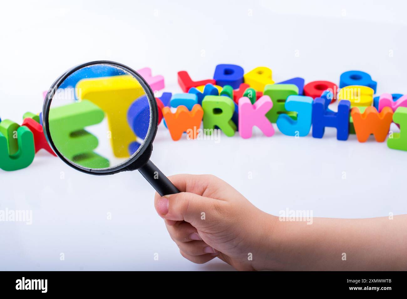 Hand holding magnifying glass over wooden alphabet letters Stock Photo