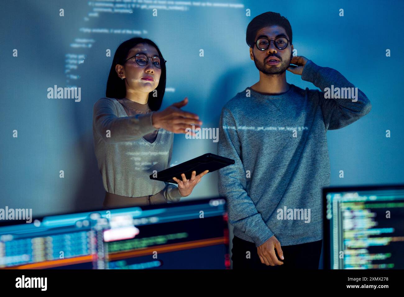 Asian Two software developers engaged in collaborative coding session, with code projected onto the wall and multiple computer screens displaying Stock Photo