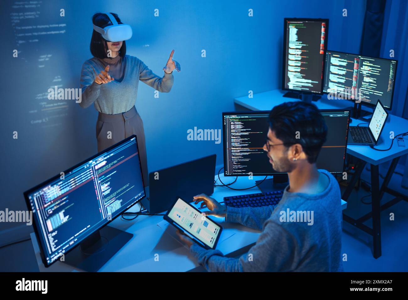 developer uses a VR headset to interact with projected interface designs, while colleagues discuss and code on screens, highlighting the integration o Stock Photo