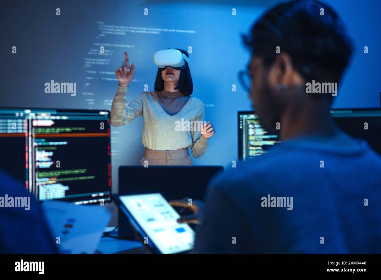 developer uses a VR headset to interact with projected interface designs, while colleagues discuss and code on screens, highlighting the integration o Stock Photo