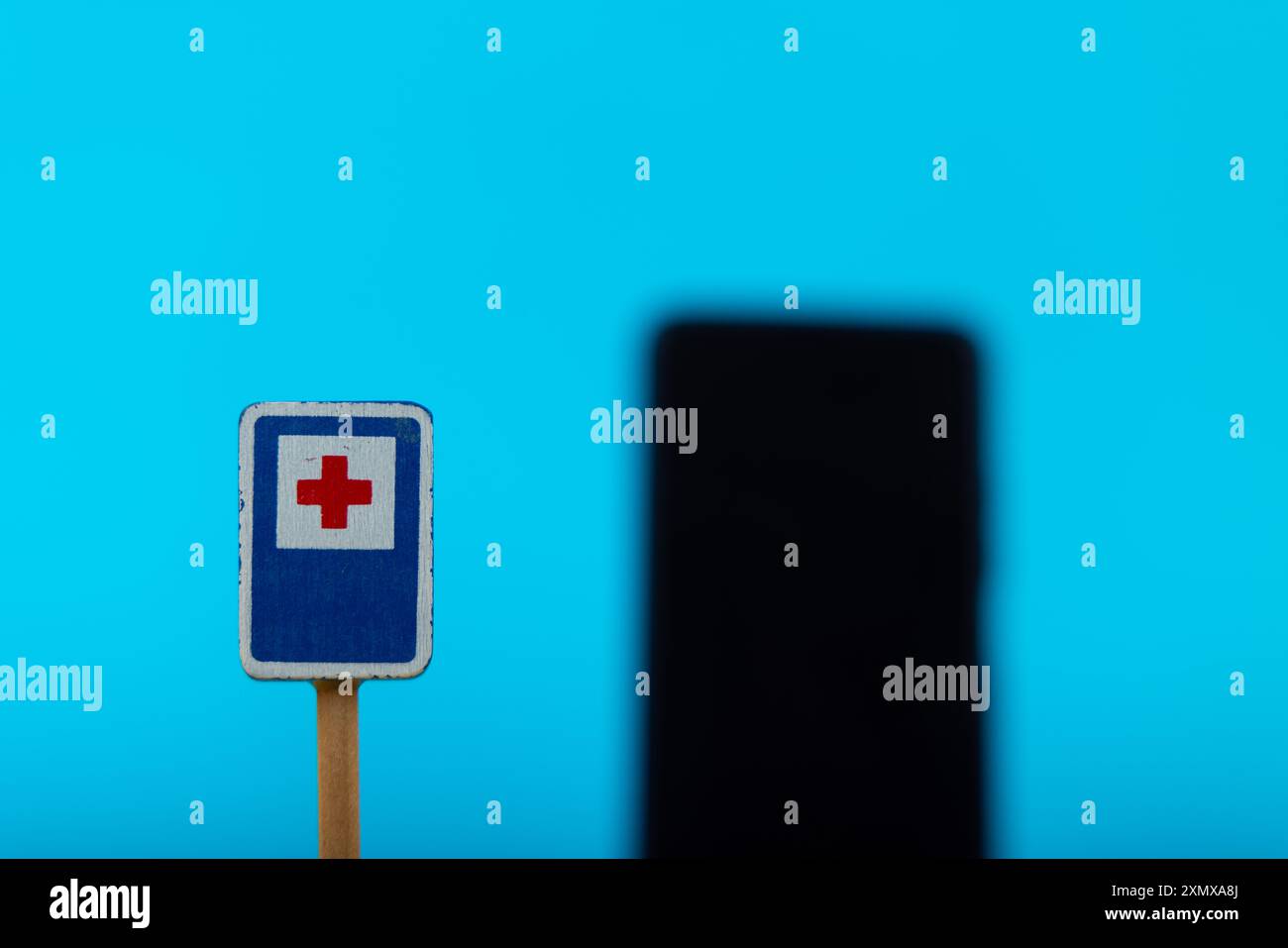 A detailed shot of a wooden toy hospital warning sign, with a smartphone slightly blurred behind it, all set on a blue background, offering a conceptu Stock Photo