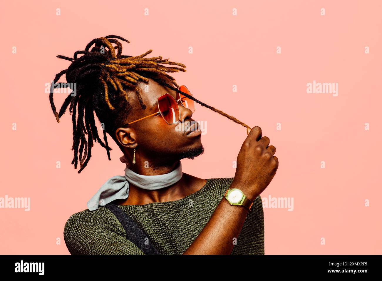 Portrait of a young man in green with dreadlocks and blue sunglasses, isolated on pink Stock Photo