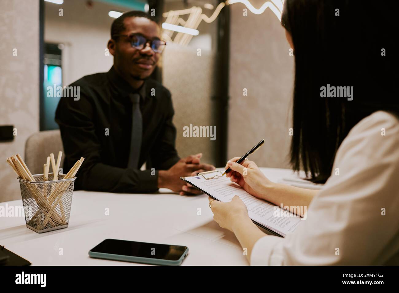 Unrecognizable HR manager making notes in document while interviewing young African American specialist Stock Photo