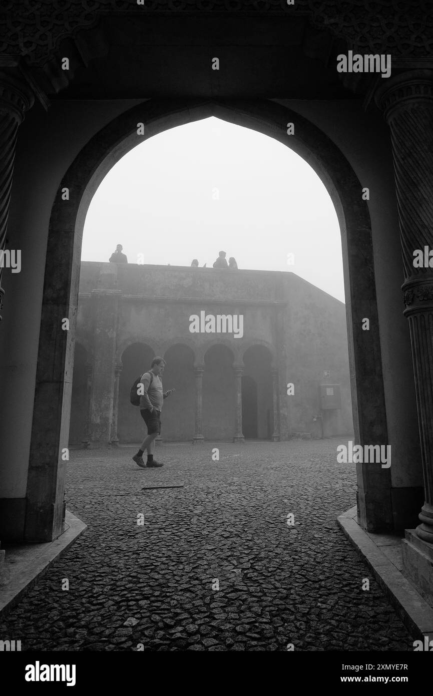 A visitor stands framed by an archway, gazing into the misty courtyard of Pena Palace Stock Photo