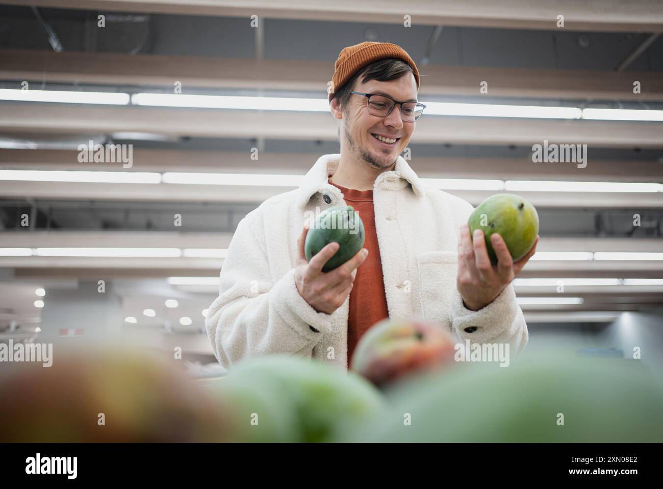 Man in beanie and warm coat smiles while selecting fresh mangoes in ...