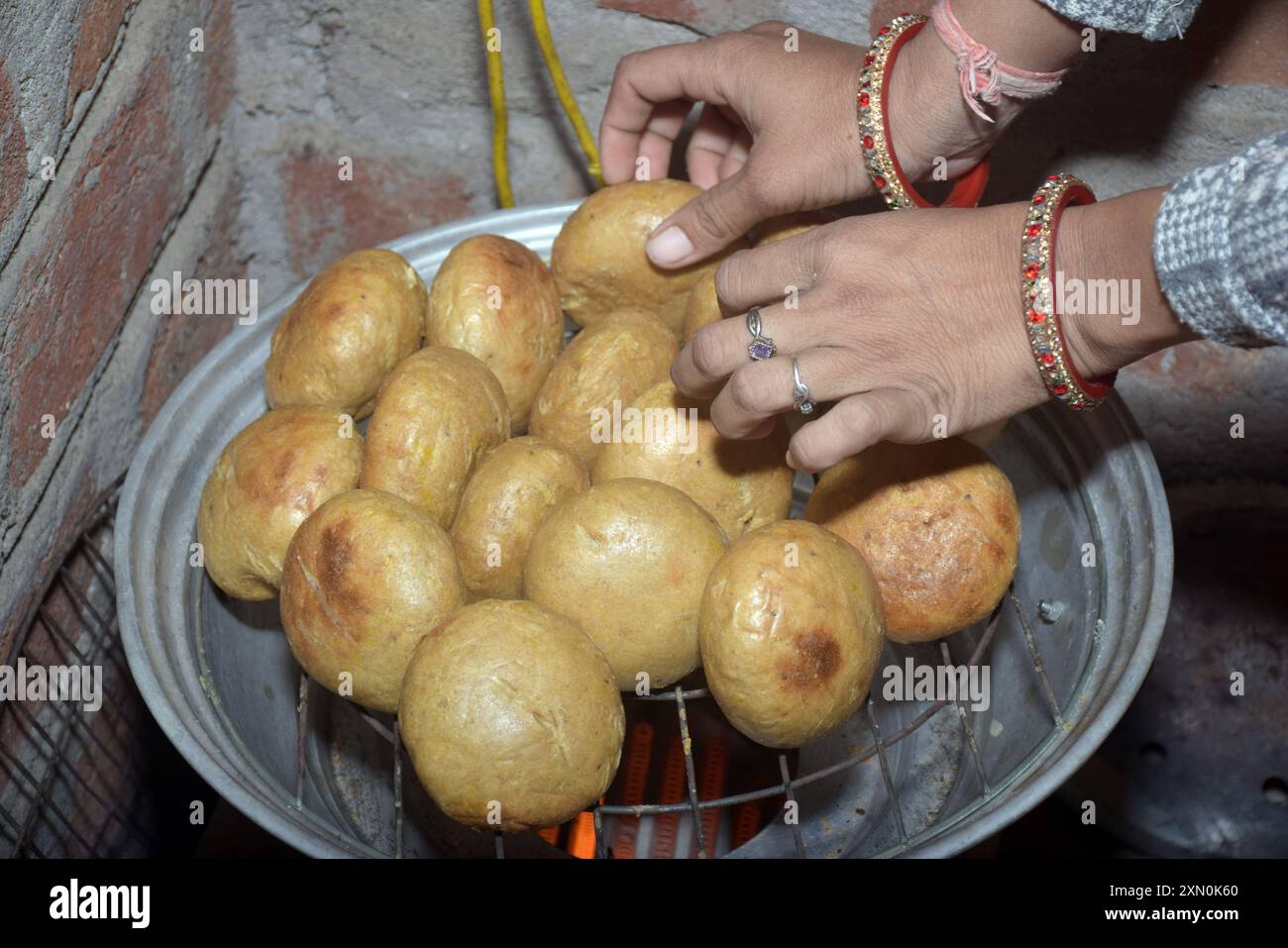 Indian housewife's hands baking on Bati oven, close-up of Rajasthani Indian dish, wheat flour balls, kitchen background. traditional unleavened bread Stock Photo