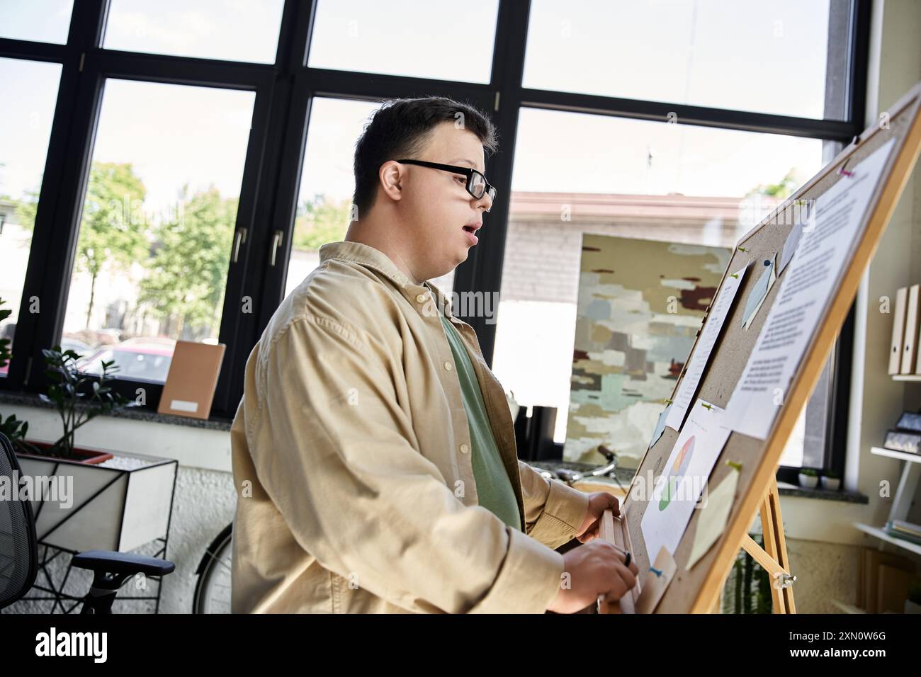 A young man with Down syndrome stands beside a presentation board, confidently sharing his ideas. Stock Photo
