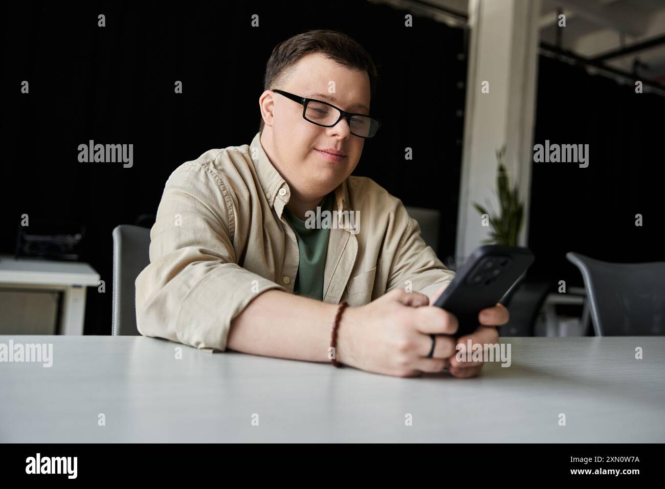 A young man with Down syndrome smiles while using his phone. Stock Photo