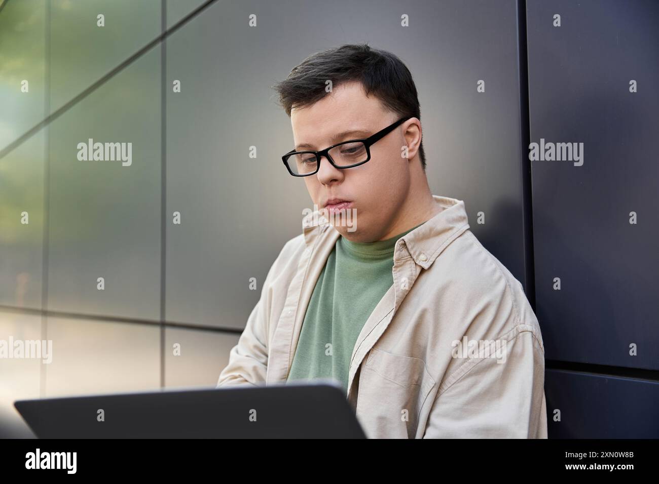 A man with Down syndrome sits outside, working on his laptop. Stock Photo