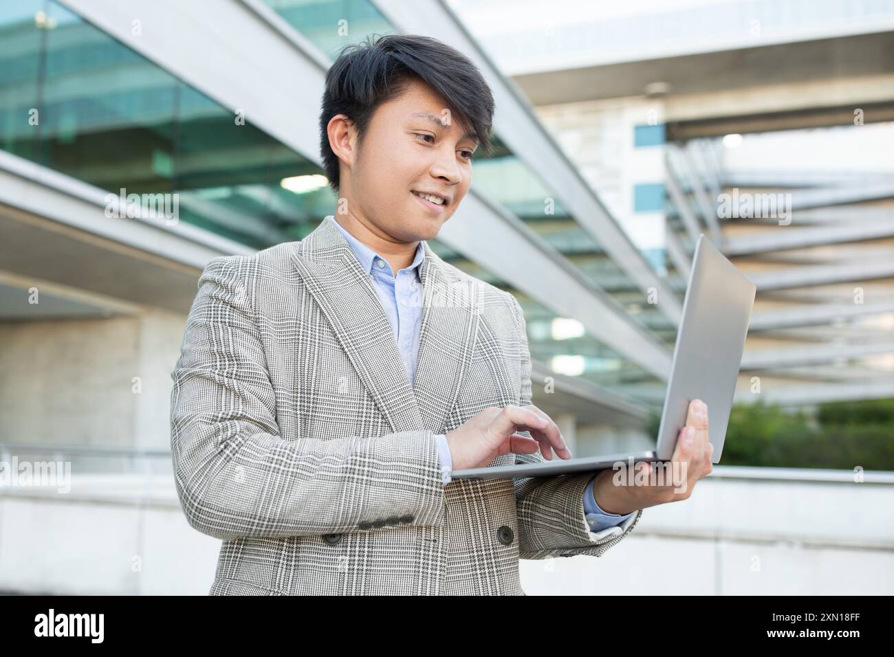 Young Asian Man Using Laptop Outside a Modern Building Stock Photo