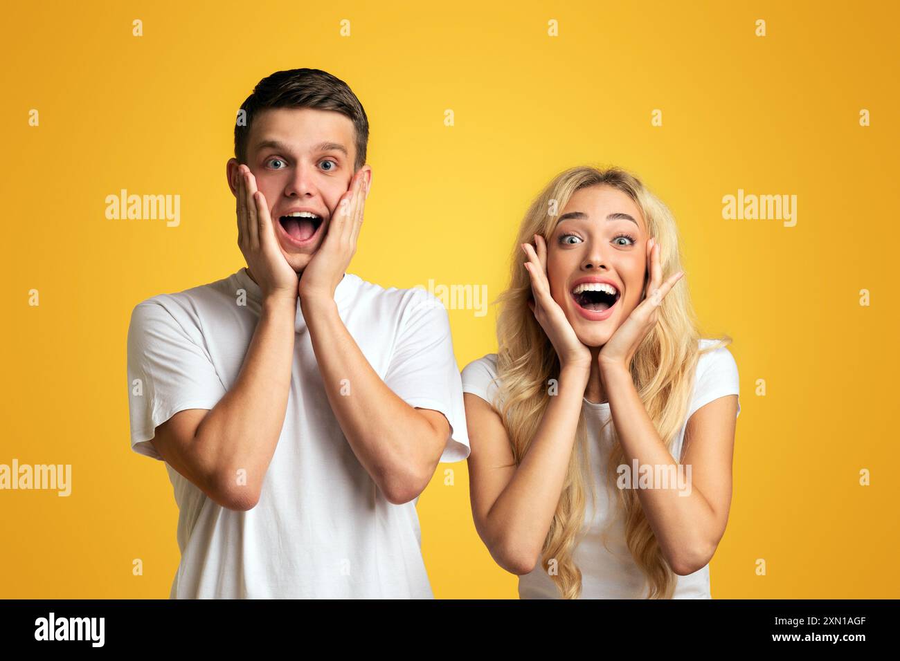 Excited young couple opening mouths and touching cheeks in amazement ...