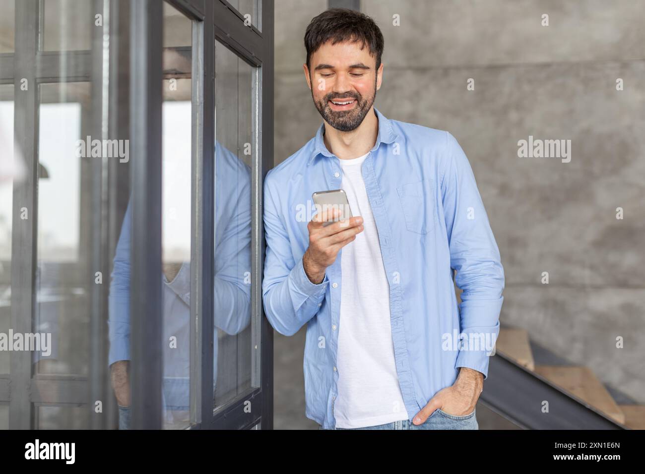 Smiling Man Using Smartphone by Glass Door Stock Photo