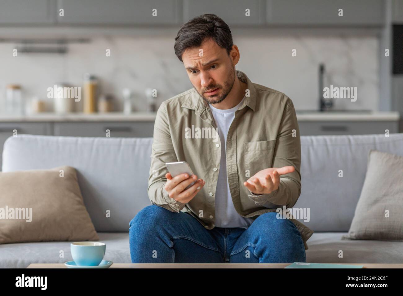 Man Expressing Confusion While Using Phone on Couch at Home Stock Photo