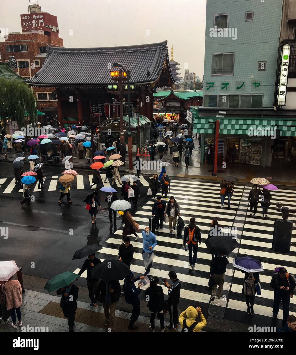 Umbrellas and people crossing a busy Tokyo street in the rain, creating a vibrant urban scene. Stock Photo