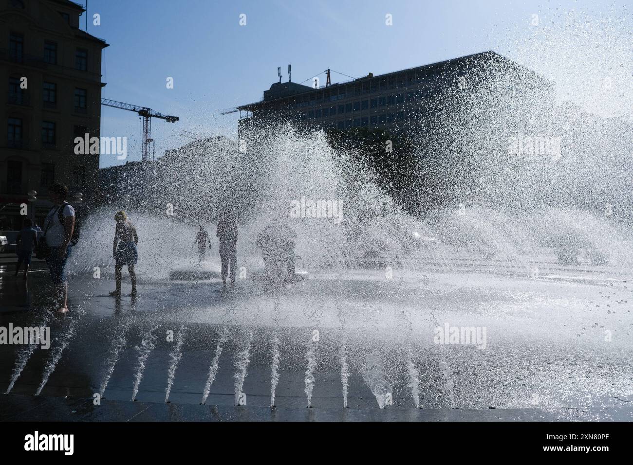 Wasserfontäne am Stachus Brunnen Stachus Brunnen im Sommer. Besucher kühlen sich in den Wasserstrahlen und Fontänen des Brunnens bei starker Hitze ab. Stock Photo