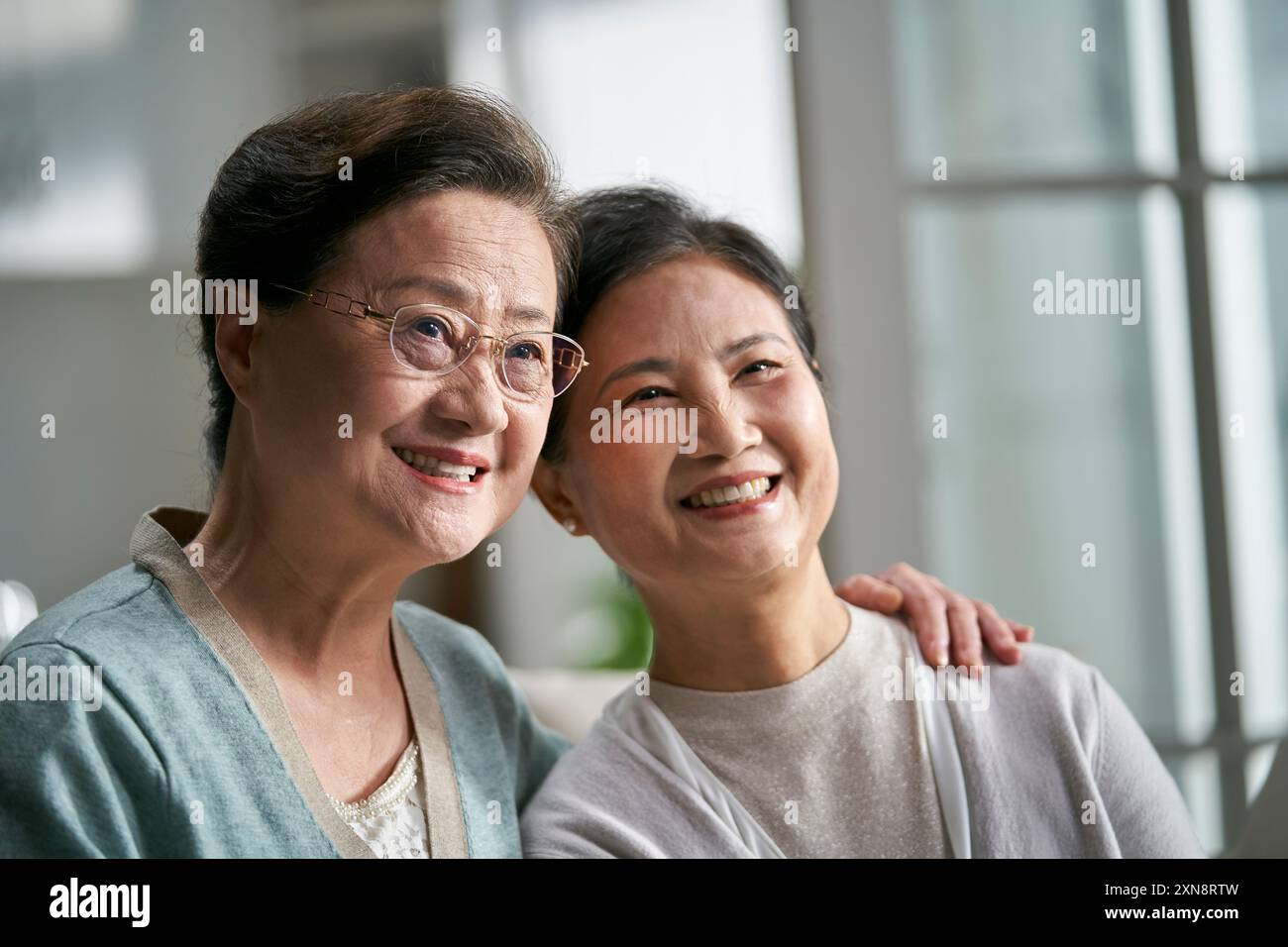 portrait of two senior asian woman sitting on couch at home happy and smiling Stock Photo